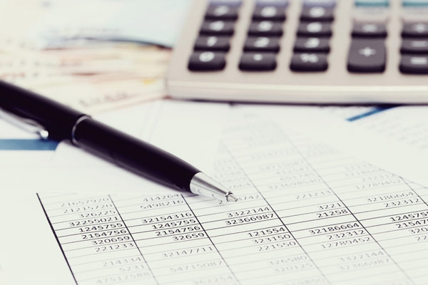 A pen resting on financial documents with numbers and graphs, next to a calculator, emphasizing accounting or budgeting tasks.