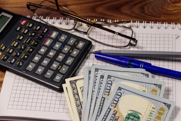 A calculator, pen, and glasses on a desk.